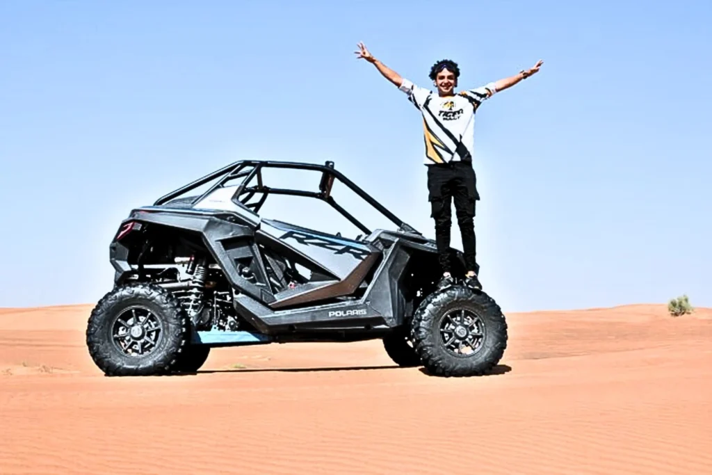 a boy standing on a 1 seater dune buggy in the desert of abu dhabi and enjoying a desert safari with 1 seater dune buggy ride