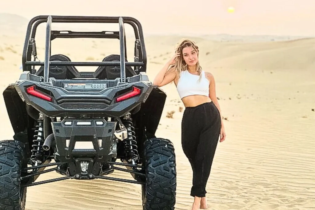 a girl standing next to a 4 seater dune buggy in the desert of abu dhabi and enjoying a desert safari with 4 seater dune buggy ride in abu dhabi